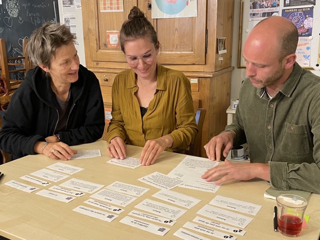 3 personnes sont assis à une table et jouent avec des cartes pour découvrir le sujet de la rencontre